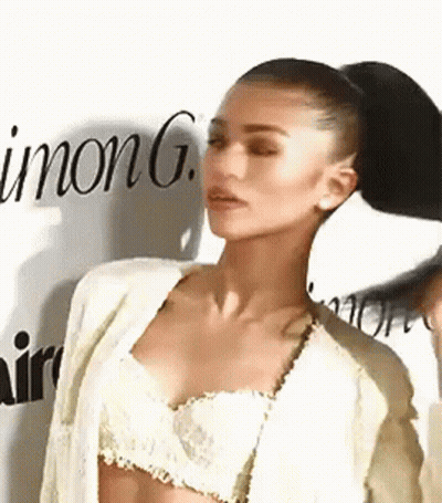 A Woman In A Crop Top And Jacket Is Standing In Front Of A Wall With The Word Inong Written On It . GIF