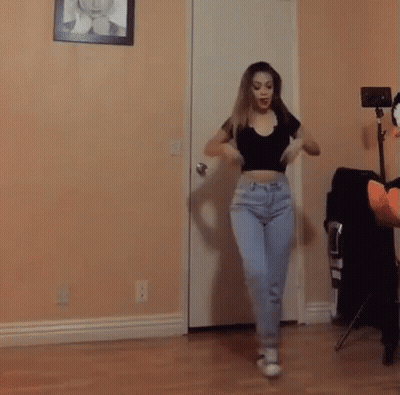 A Woman In A Crop Top And Jeans Is Dancing In A Room . GIF