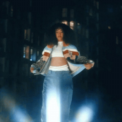 A Woman In A Crop Top And Jeans Is Standing In Front Of A Building GIF
