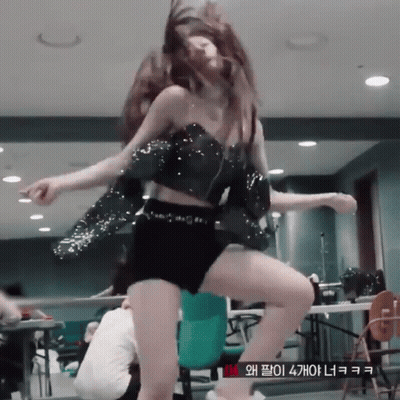 A Woman In A Crop Top And Shorts Is Dancing In A Room With A Sign That Says Vm GIF
