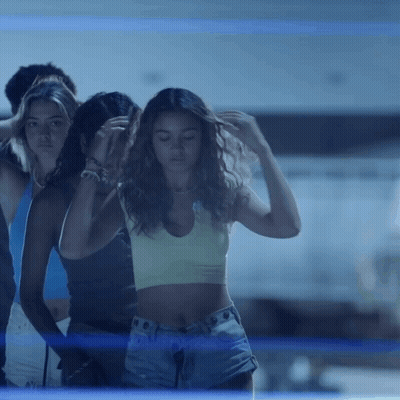 A Woman In A Crop Top And Shorts Stands In Front Of A Group Of People GIF