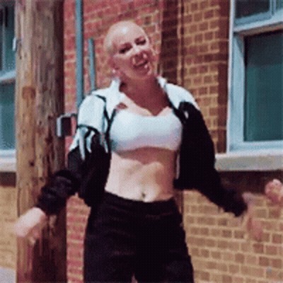 A Woman In A Crop Top Is Dancing In Front Of A Brick Wall GIF