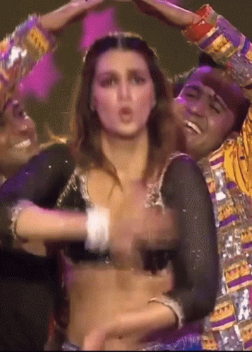 A Woman In A Crop Top Is Dancing With A Man In A Colorful Outfit . GIF