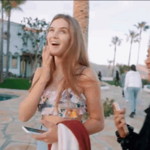 A Woman In A Crop Top Is Laughing While Holding A Cell Phone In Her Hand . GIF