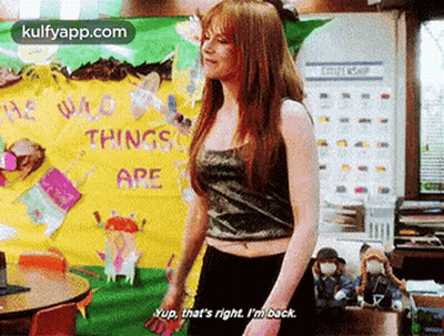 A Woman In A Crop Top Is Standing In Front Of A Bulletin Board That Says `` He Who Things Are '' . GIF