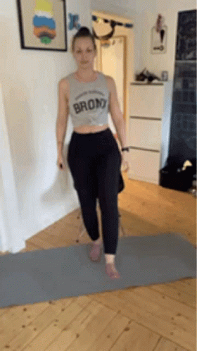 A Woman In A Crop Top Is Standing On A Yoga Mat . GIF