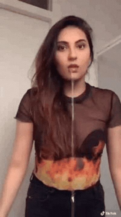 A Woman In A Crop Top With Flames On It Is Standing In Front Of A Door With Her Mouth Open . GIF