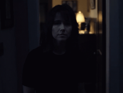 A Woman In A Dark Room With A Lamp In The Background GIF