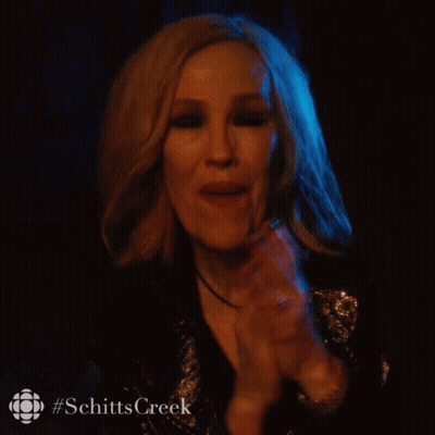 A Woman In A Dark Room With #Schittscreek Written On The Bottom Right GIF