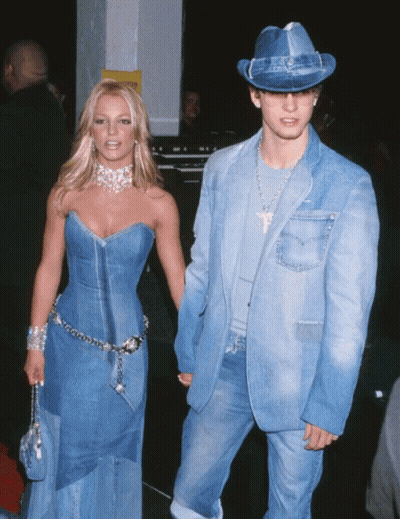 A Woman In A Denim Dress Holds Hands With A Man In A Denim Suit And Hat GIF