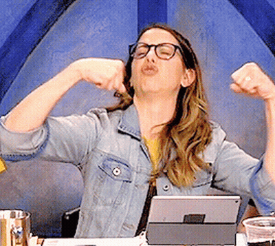 A Woman In A Denim Jacket And Glasses Is Flexing Her Muscles In Front Of A Tablet GIF