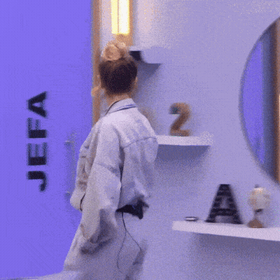 A Woman In A Denim Jacket And Pants Stands In Front Of A Blue Wall GIF