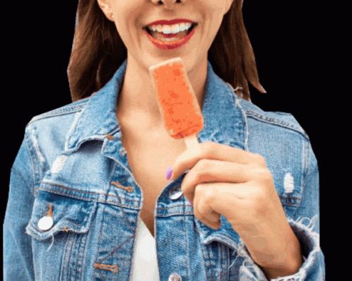 A Woman In A Denim Jacket Is Holding An Orange Popsicle GIF