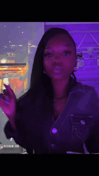 A Woman In A Denim Jacket Is Standing In Front Of A Window With A Purple Light Behind Her . GIF
