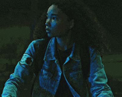 A Woman In A Denim Jacket Is Standing In The Dark . GIF