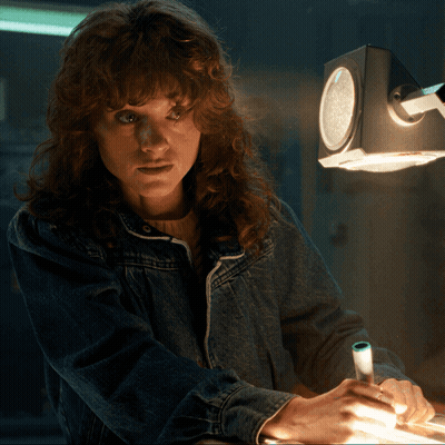 A Woman In A Denim Jacket Is Writing On A Piece Of Paper Under A Clock GIF