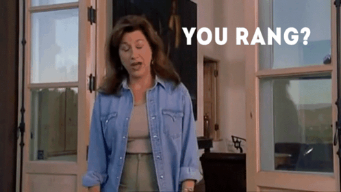 A Woman In A Denim Shirt Is Standing In Front Of A Door With The Words " You Rang " On The Bottom GIF
