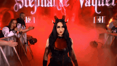 A Woman In A Devil Costume Stands In Front Of A Sign That Says ' Stephanie Vaughn ' GIF