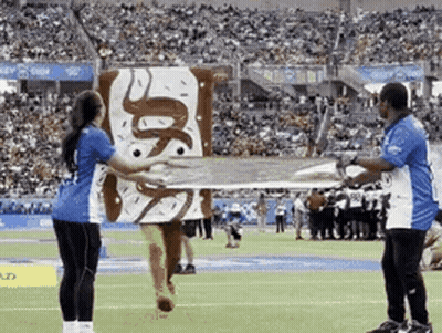 A Woman In A Donut Costume Is Holding A Large Donut On A Field GIF
