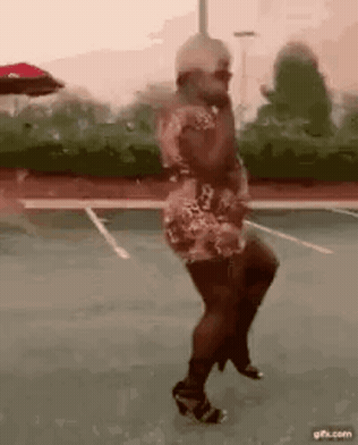 A Woman In A Dress And High Heels Is Dancing On A Parking Lot . GIF