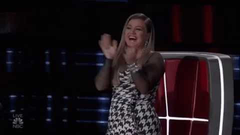 A Woman In A Dress Is Sitting In A Chair And Clapping Her Hands . GIF