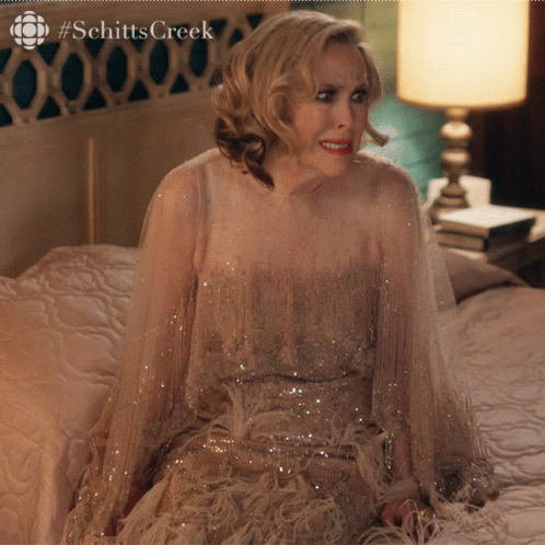 A Woman In A Dress Is Sitting On A Bed With #Schitts Creek On The Bottom GIF