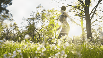 A Woman In A Dress Is Standing In A Field Of White Flowers GIF