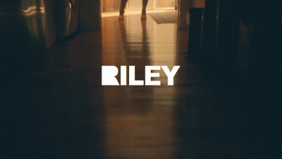 A Woman In A Dress Is Standing In A Hallway With The Word Riley On The Bottom GIF