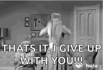 A Woman In A Dress Is Standing In A Living Room With A Man Sitting On A Couch . GIF