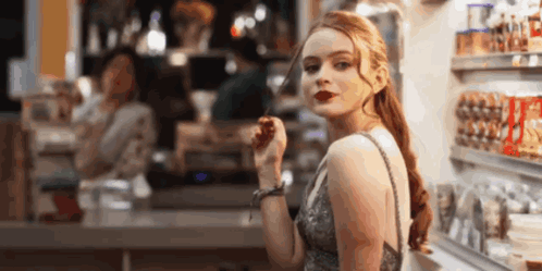 A Woman In A Dress Is Standing In Front Of A Counter In A Store Eating A Candy Bar . GIF
