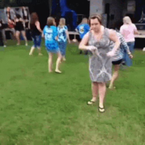A Woman In A Dress Is Standing In The Grass Holding A Frisbee . GIF