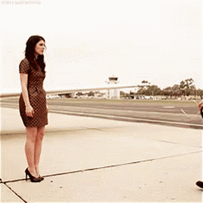 A Woman In A Dress Is Standing Next To A Man On A Runway GIF
