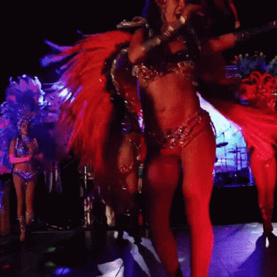 A Woman In A Feathered Costume Is Dancing In A Dark Room GIF