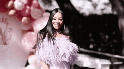 A Woman In A Feathered Dress Is Standing In Front Of Balloons And Smiling . GIF