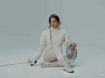 A Woman In A Fencing Outfit Is Kneeling Down Holding A Sword And A Helmet GIF