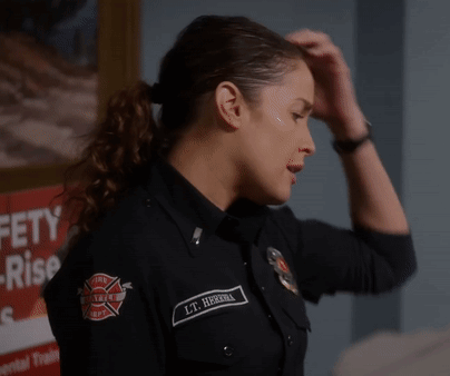 A Woman In A Firefighter Uniform Has Her Hand On Her Head In Front Of A Sign That Says Safety Rise GIF