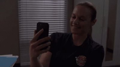 A Woman In A Firefighter Uniform Is Taking A Selfie With Her Cell Phone GIF