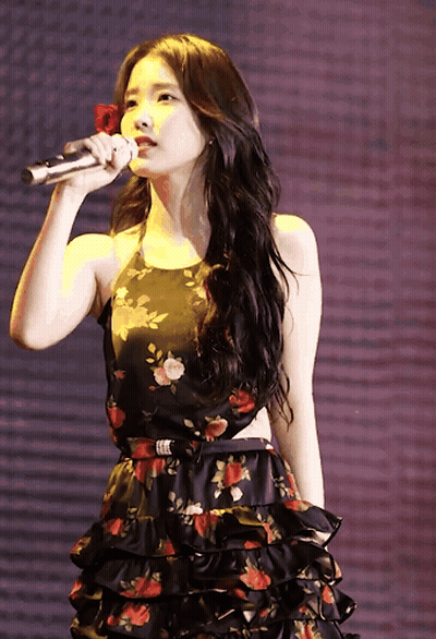 A Woman In A Floral Dress Holds A Microphone In Her Hand GIF