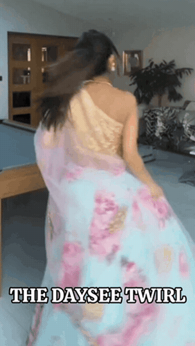 A Woman In A Floral Dress Is Dancing In A Room With The Words The Daysee Twirl Above Her GIF