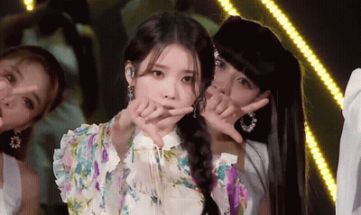 A Woman In A Floral Dress Is Making A Heart Shape With Her Fingers GIF