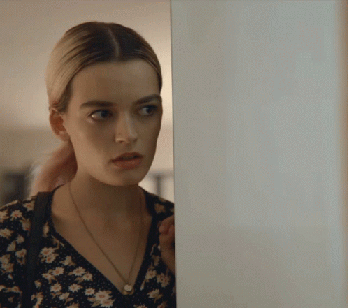 A Woman In A Floral Dress Is Peeking Behind A Door GIF