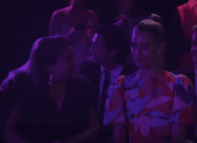 A Woman In A Floral Dress Talks To A Man In A Suit GIF