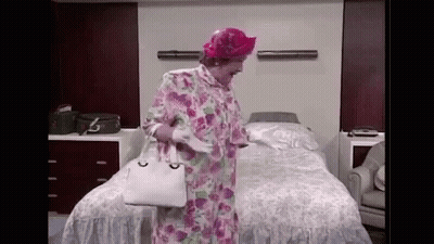 A Woman In A Floral Robe And Pink Hat Is Standing In Front Of A Bed In A Hospital Room . GIF