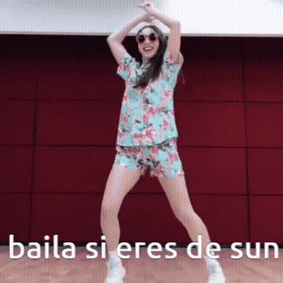 A Woman In A Floral Shirt And Shorts Is Dancing With The Words Baila Si Eres De Sun Above Her GIF