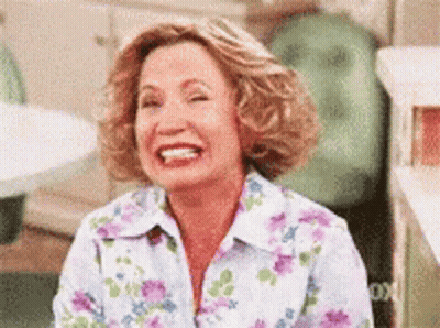 A Woman In A Floral Shirt Is Laughing While Sitting Down . GIF