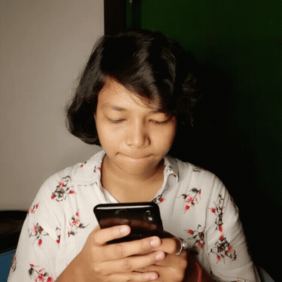 A Woman In A Floral Shirt Is Looking At A Cell Phone GIF