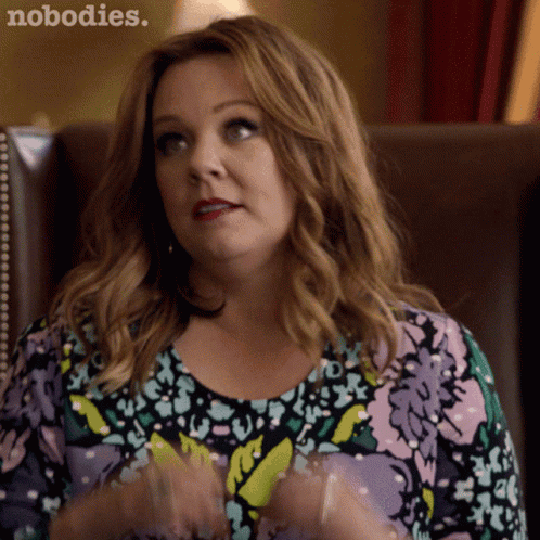 A Woman In A Floral Shirt Is Sitting In A Chair With The Words Nobodies Written On The Bottom GIF