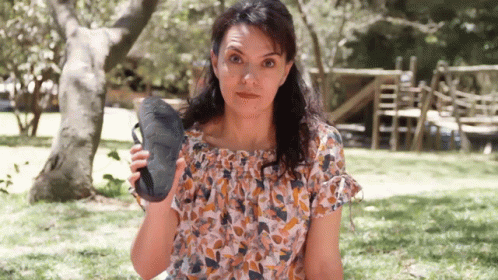 A Woman In A Floral Top Is Holding A Pair Of Shoes GIF