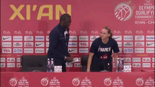 A Woman In A France Shirt Stands In Front Of A Xian Sign GIF