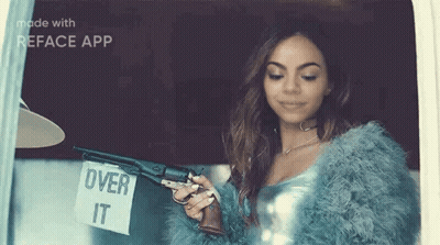 A Woman In A Fur Coat Is Holding A Gun And A Sign That Says `` Over It '' . GIF